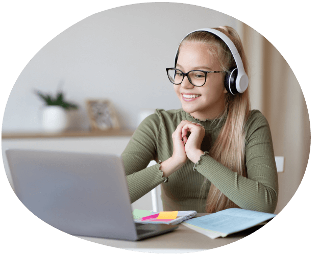 Mädchen mit Kopfhörern vor Laptop und Schulheften am Schreibtisch, zufriedener Blick auf den Bildschirm